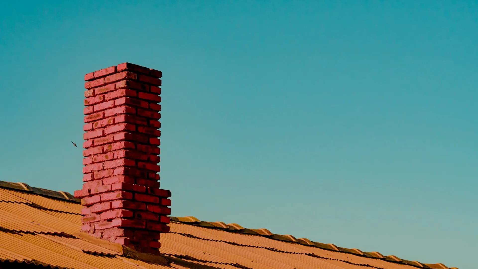 Brick chimney rising from a tile roof at sunset